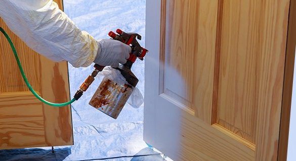 A professional painter wearing safety uniform and gloves applying polish on the doors by using a mechanized tool.